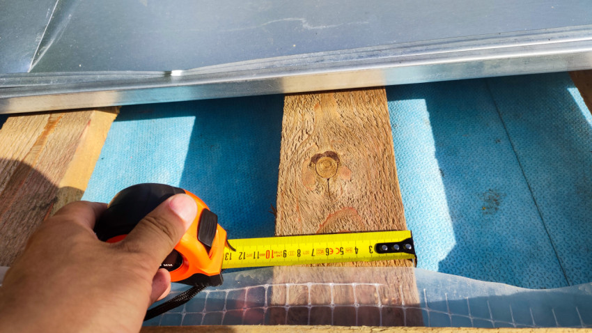 Замер расстояния строительной рулеткой при монтаже крыши