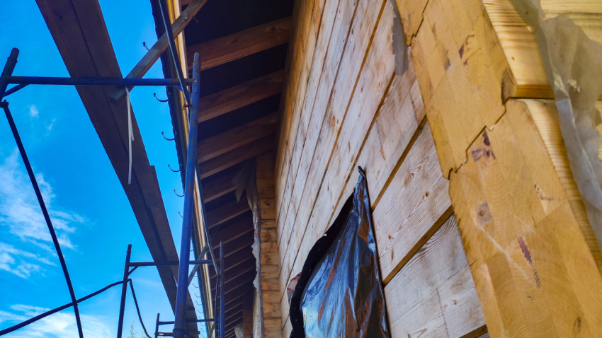 Фасад деревянного дома с лесами и установленными кронштейнами под водосток