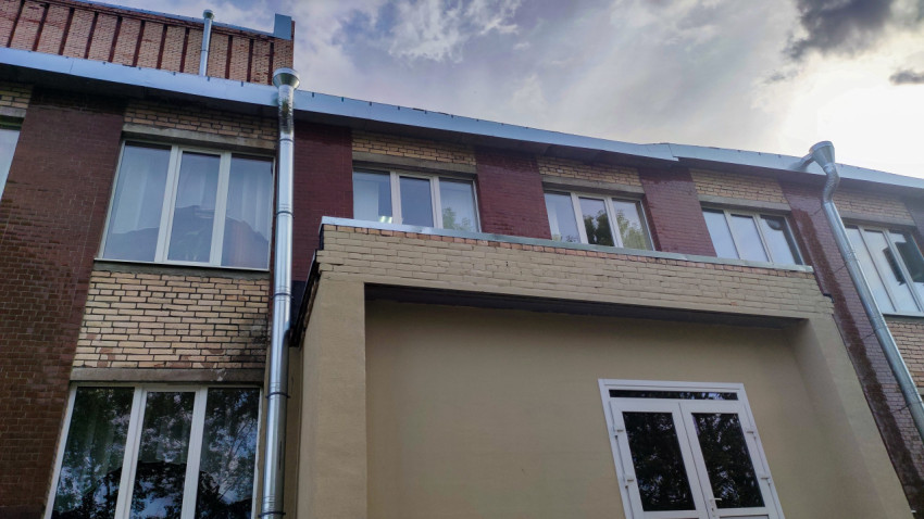 Участок фасада кирпичного здания с водосточной системой и плоской кровлей