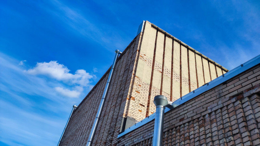 Кирпичный фасад здания с водосточными трубами на фоне голубого неба