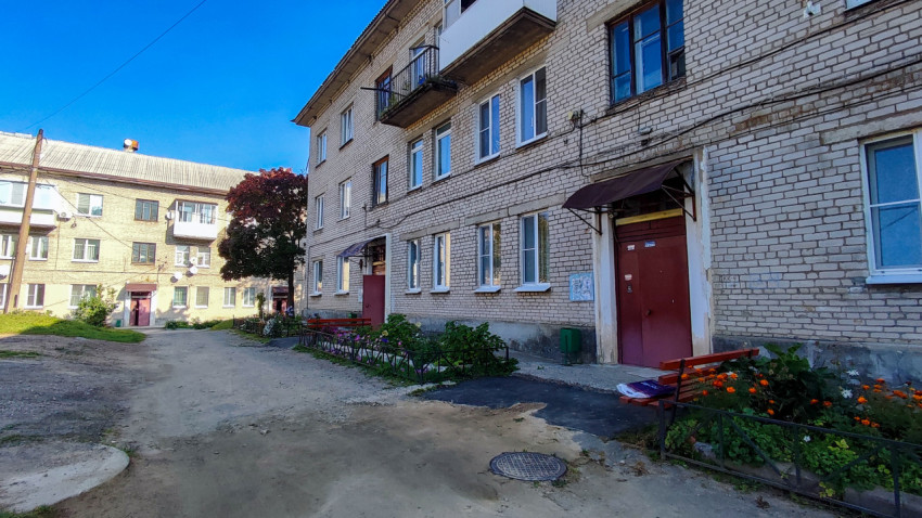 Подъезд жилого дома с цветником и лавочкой во дворе