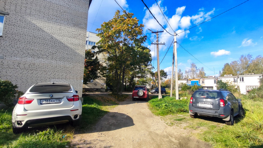 Двор между жилыми домами с опорами электросети и припаркованными автомобилями