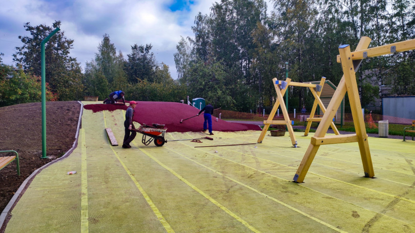 Рабочие наносят резиновое покрытие на детской площадке