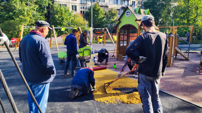 Рабочие укладывают резиновое покрытие на детской площадке