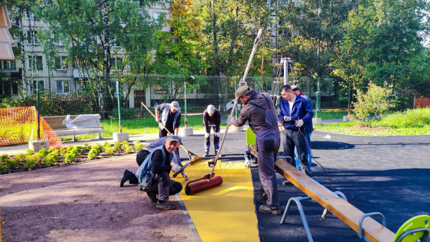 Рабочие укладывают покрытие на детской площадке во дворе