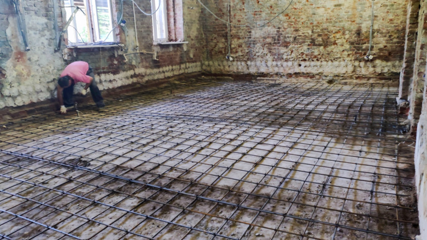 Рабочий закрепляет арматуру пола в помещении старого здания