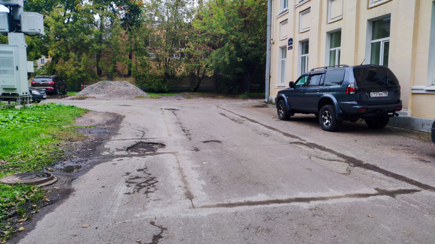 Участок с повреждённым асфальтом и складом щебня у здания