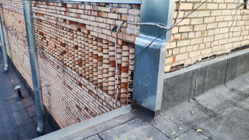 Кирпичная стена здания с инженерными коммуникациями и металлическим коробом