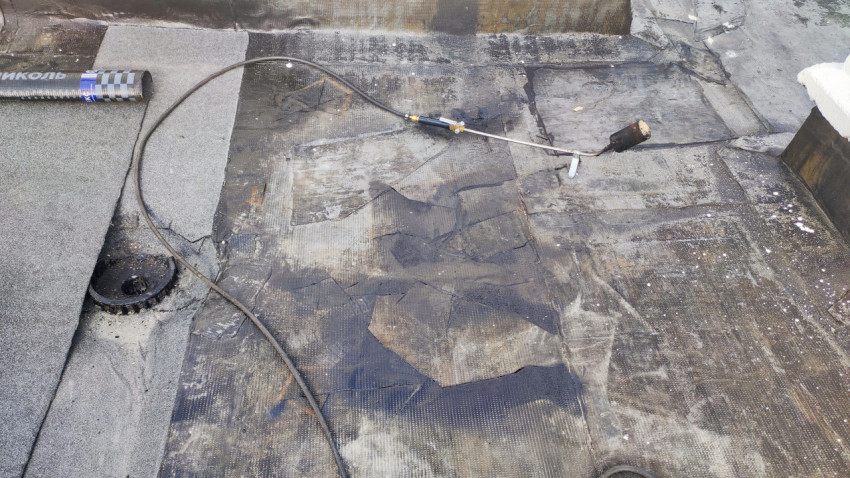 Повреждённый участок кровли с горелкой и материалами для ремонта