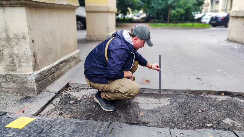 Специалист измеряет глубину снятого слоя асфальта у арки здания