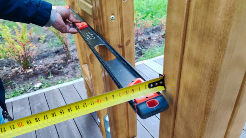 Измерение расстояния между деревянными стойками рулеткой и уровнем