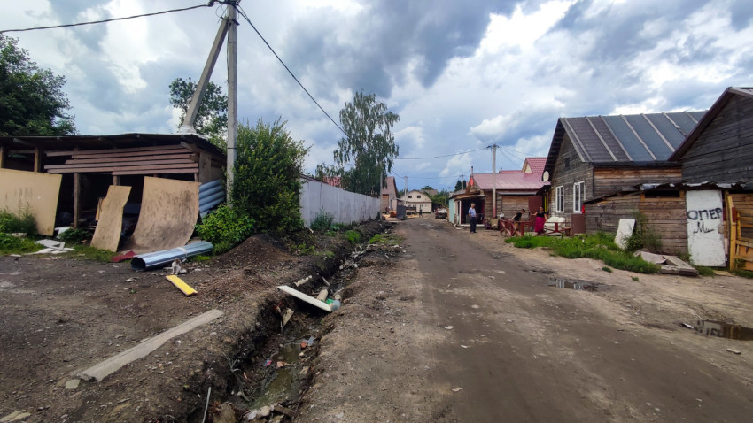 Грунтовая улица с жилыми домами и открытой канавой