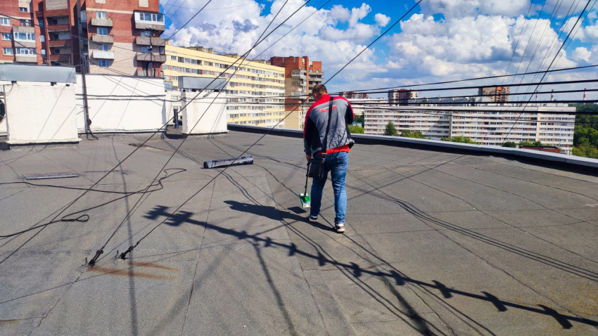 Специалист обследует крышу многоквартирного дома с влагомером