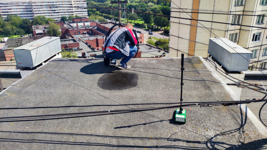 Специалист на крыше многоквартирного дома рядом с влагомером