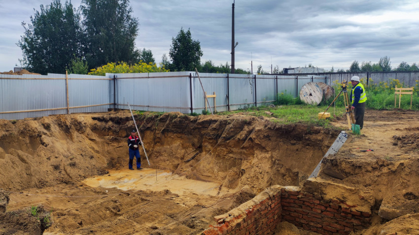 Рабочий с рейкой и геодезист у котлована