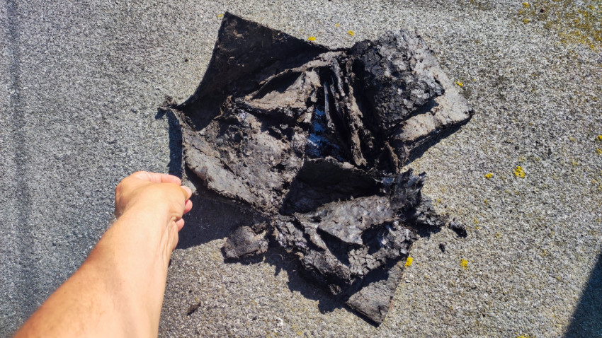 Человек поднимает повреждённый слой кровли