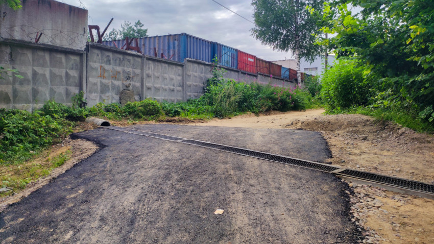 Асфальтированная дорога с дренажным каналом у бетонного забора