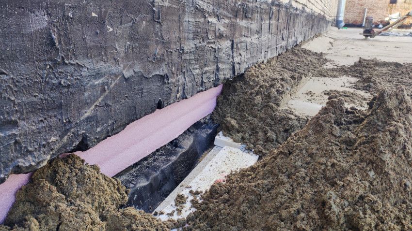 Утеплитель и песчаная засыпка у кирпичной стены здания