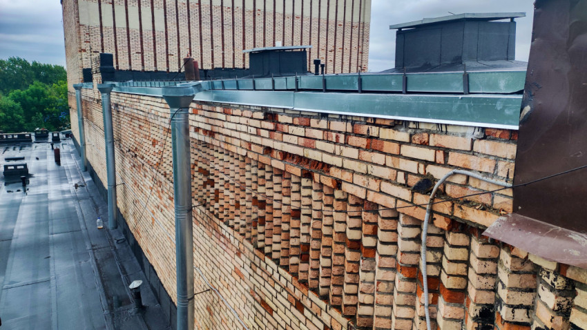 Кирпичная стена здания с водосточными трубами и кровлей