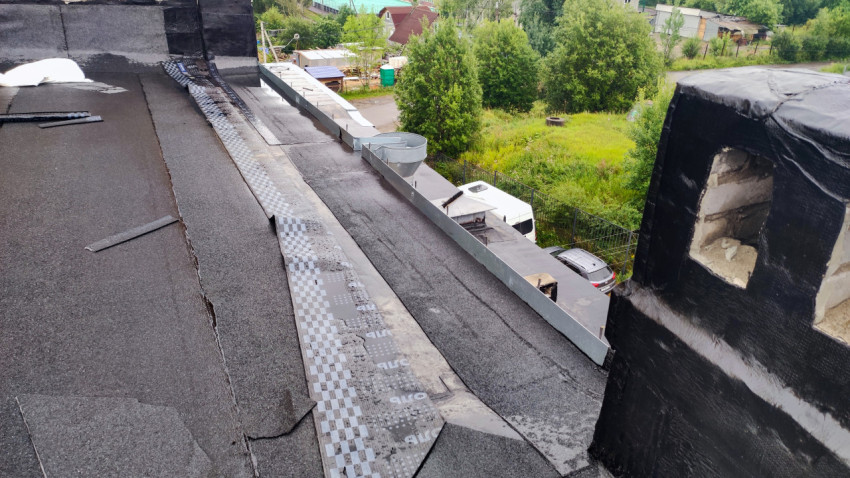 Кровля здания с водосточной системой и частным сектором на заднем плане