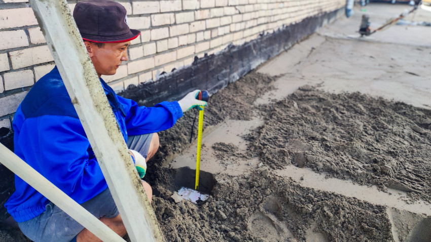 Рабочий измеряет слой стяжки у кирпичной стены