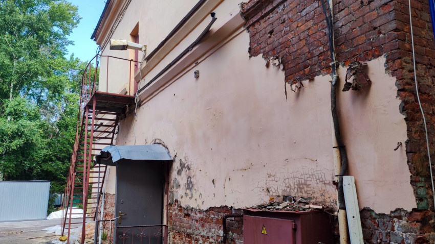 Кирпичная стена здания с металлической лестницей и повреждённой штукатуркой