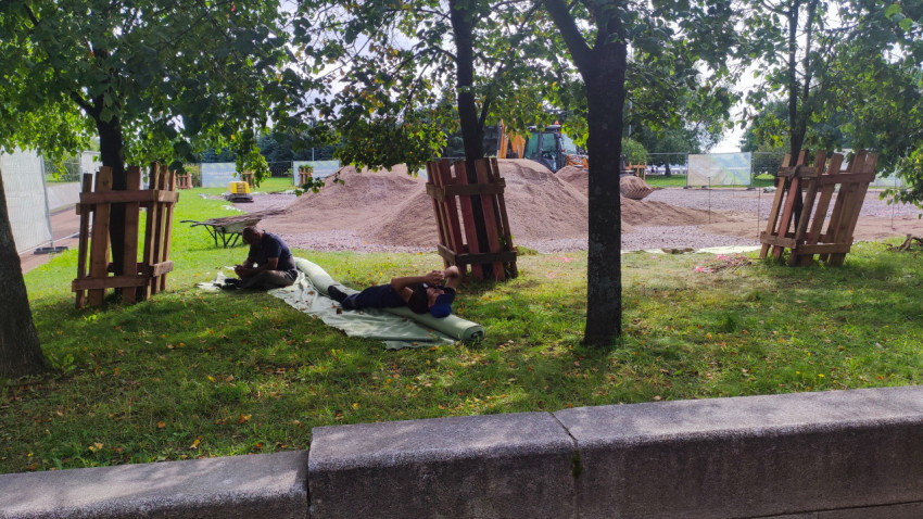 Рабочие отдыхают в тени деревьев на строительной площадке