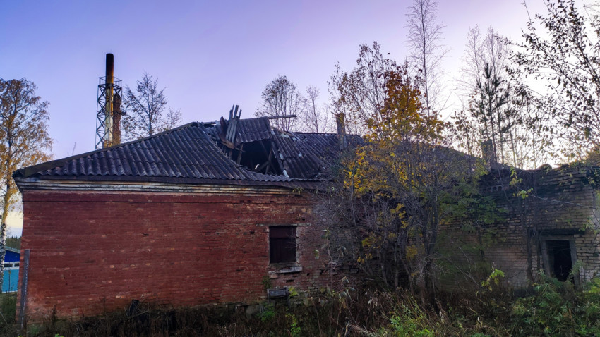 Разрушенное здание с проваленной крышей и кирпичной трубой на фоне заката