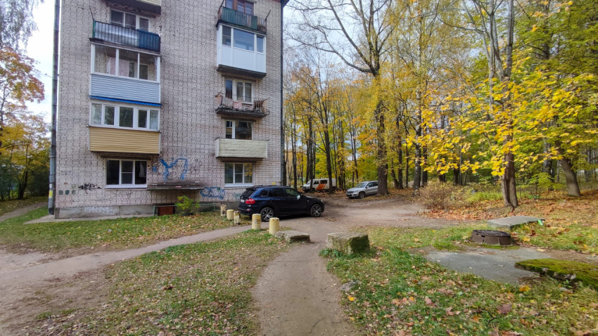 Конец жилого дома и двор с припаркованными автомобилями среди осенних деревьев