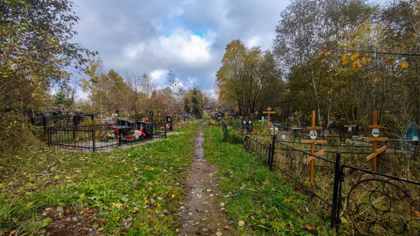 Осенняя дорога через кладбище с металлическими оградами