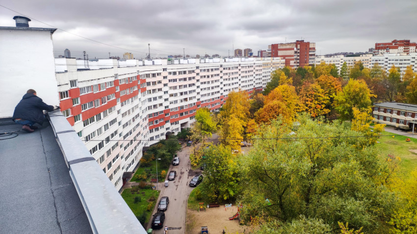 Рабочий у парапета на плоской кровле многоквартирного дома