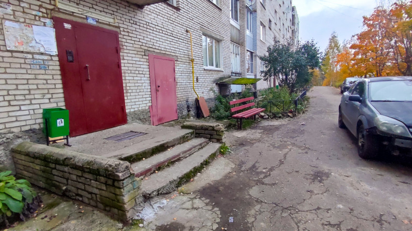 Подъезд жилого дома с лавочкой и автомобилем во дворе