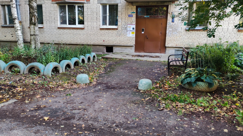 Подъезд жилого дома с клумбами из шин и лавочкой