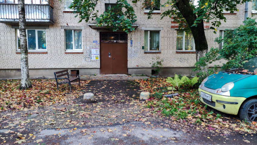 Вход в подъезд жилого дома с лавочкой и припаркованным автомобилем