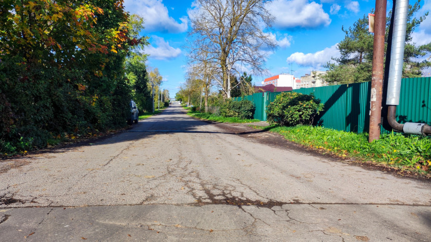 Асфальтовая улица с повреждениями покрытия и зелёными заборами