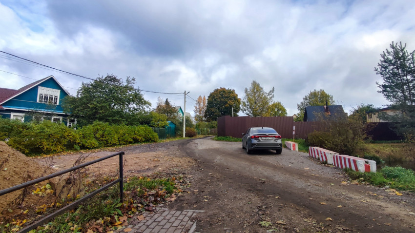 Грунтовая дорога у жилых домов с автомобилем на фоне осеннего неба