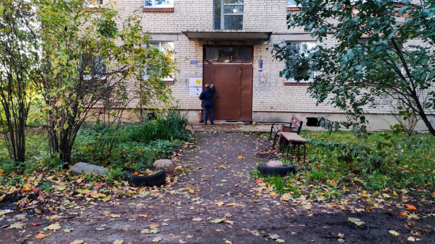 Подъезд жилого дома с человеком у двери и осенней листвой