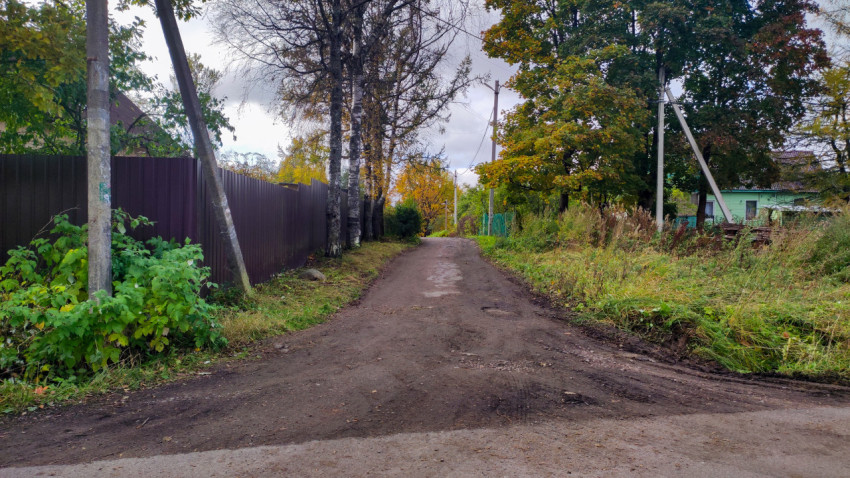Грунтовая дорога вдоль заборов и деревьев с опорами электросетей