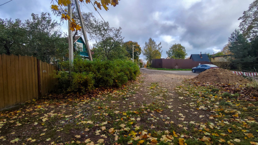 Осенняя улица с забором и легковым автомобилем у поворота деревенской дороги