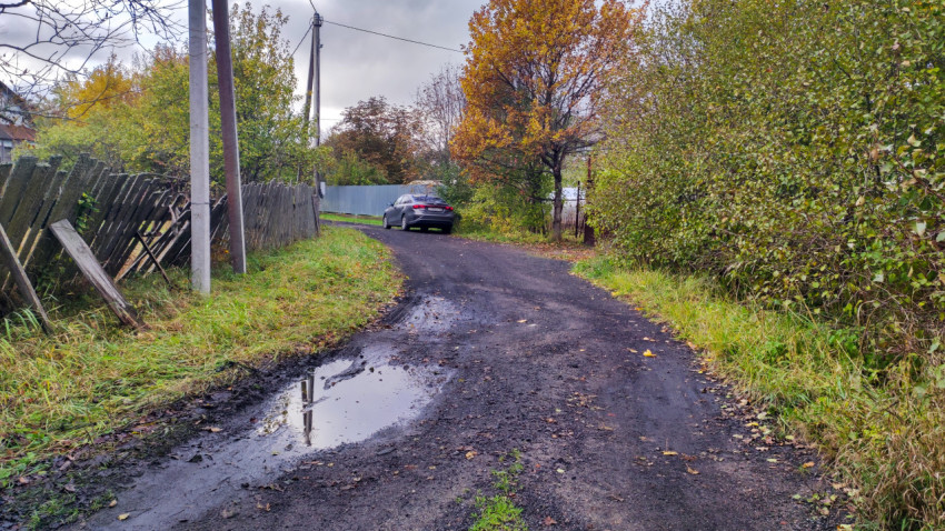 Грунтовая улица с автомобилем и деревянным забором