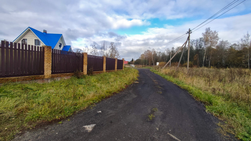 Загородная дорога вдоль кирпичного забора с домом