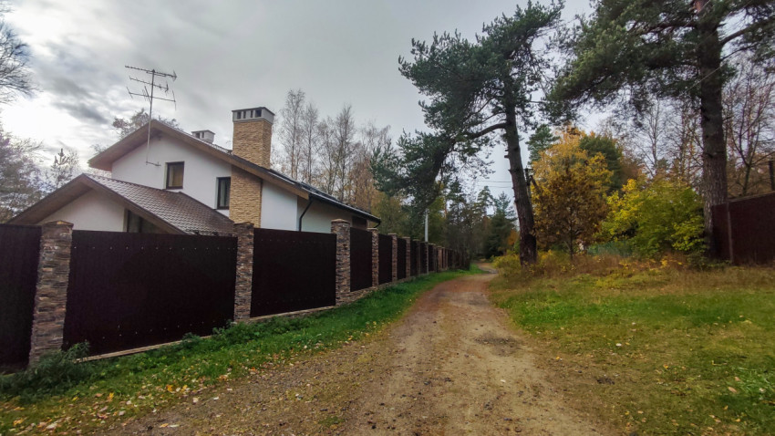 Загородный дом с каменным забором и грунтовой дорогой