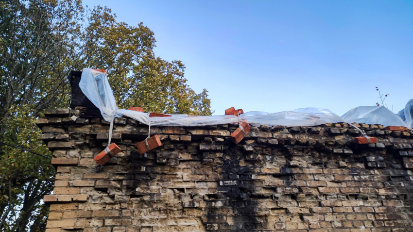 Разрушенная кирпичная стена с плёнкой и зафиксированными кирпичами