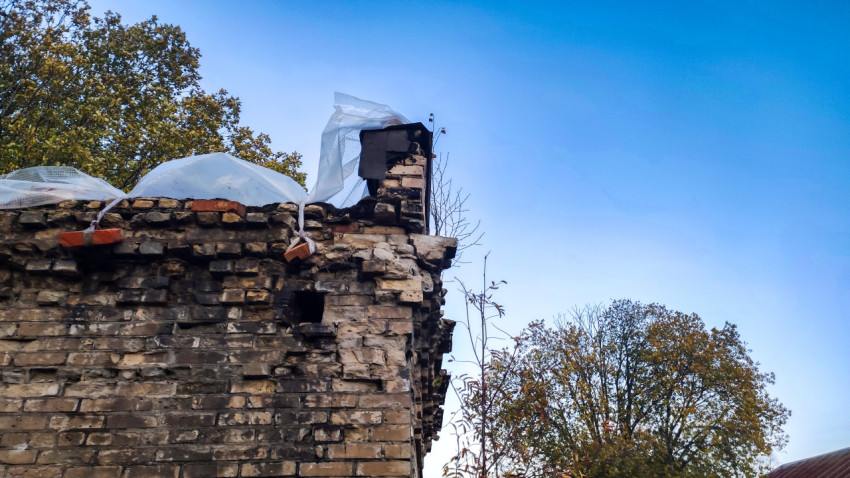 Верхняя часть разрушенной кирпичной стены с парапетом и закопчёнными кирпичами