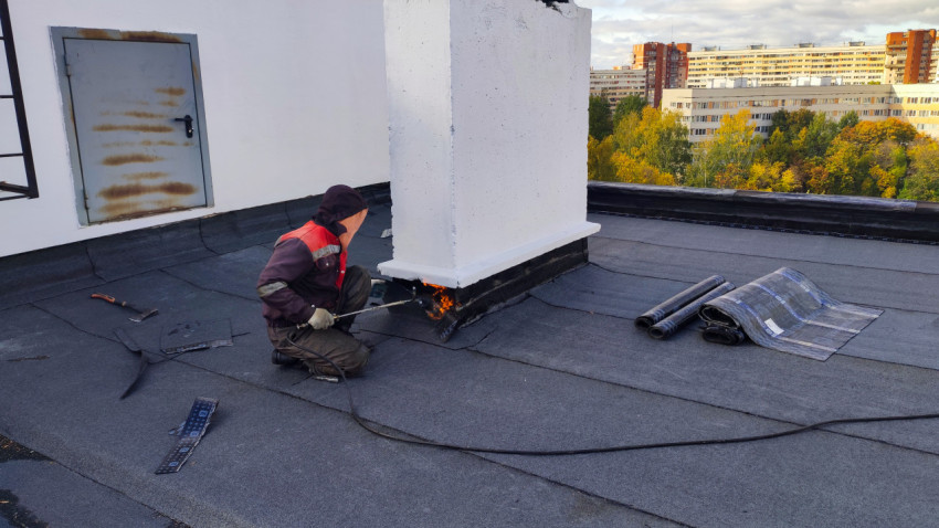 Рабочий выполняет наплавление рулонной кровли у основания шахты