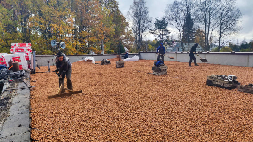 Рабочие распределяют керамзитовый гравий на плоской кровле