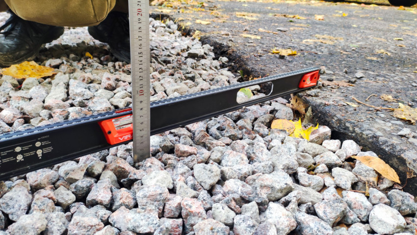 Замер расстояния от щебня до кромки асфальта с использованием уровня