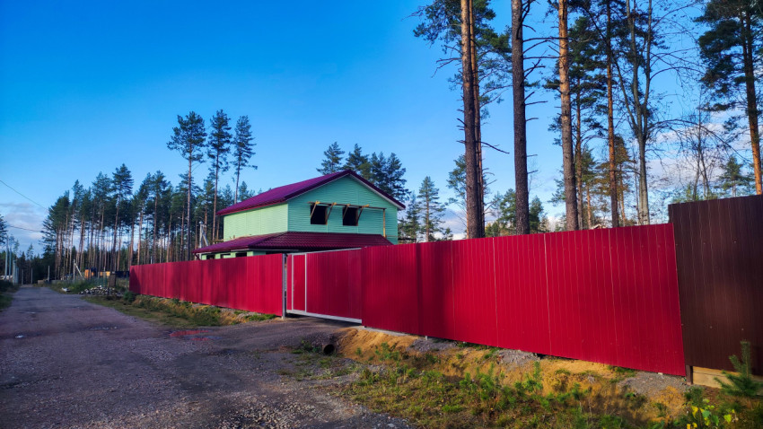 Загородный дом с красной крышей и высоким забором из профнастила