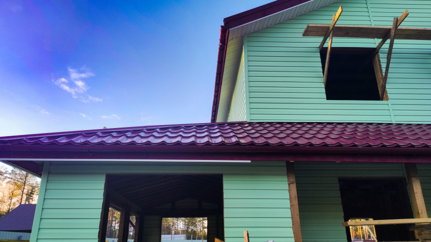 Фасад строящегося дома с зелёным сайдингом и кровлей из металлочерепицы