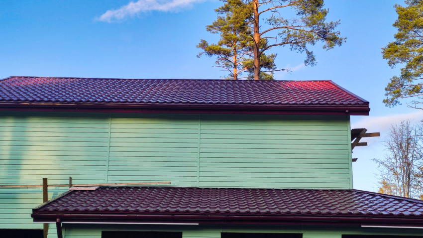 Кровля и фасад загородного дома с зелёной облицовкой и бордовой металлочерепицей